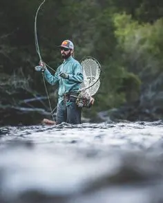 An angler casting a fishing rod into a serene lake surrounded by lush greenery and mountains, illustrating the importance of proper casting techniques in successful fishing.